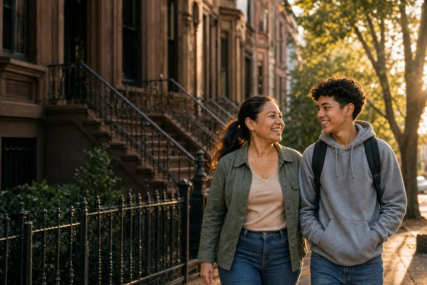 A mother and her teenage son laughing as they walk past brownstones in Queens.